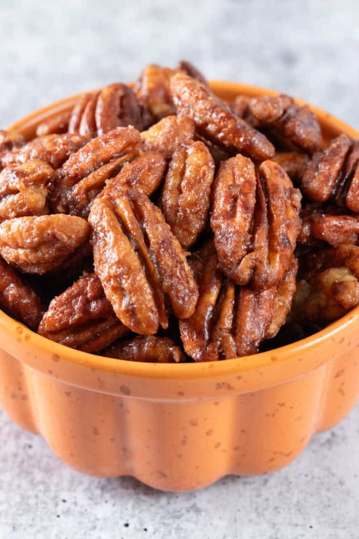 Close up view of maple candied pecans in an orange pumpkin shaped bowl.