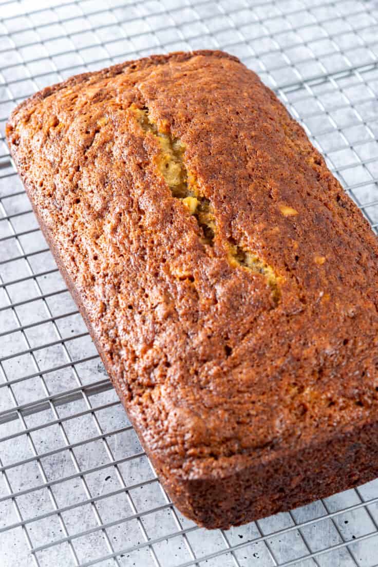 A full loaf of uncut banana bread cooling on a wire rack.