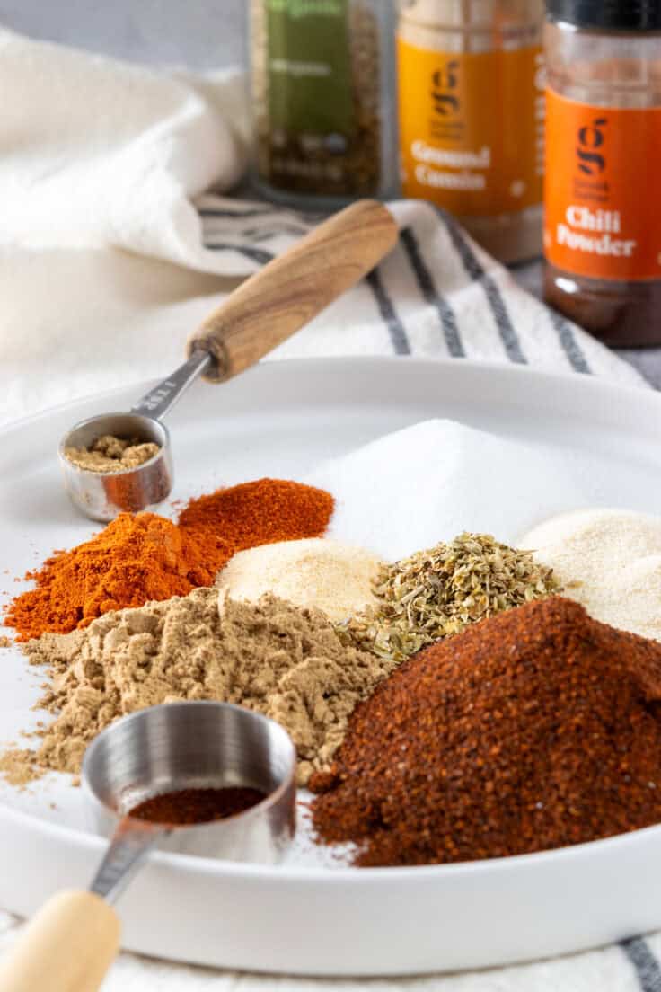 All the spices need to make homemade chili seasoning piled on a plate which is in front of bottles of the individual spices.