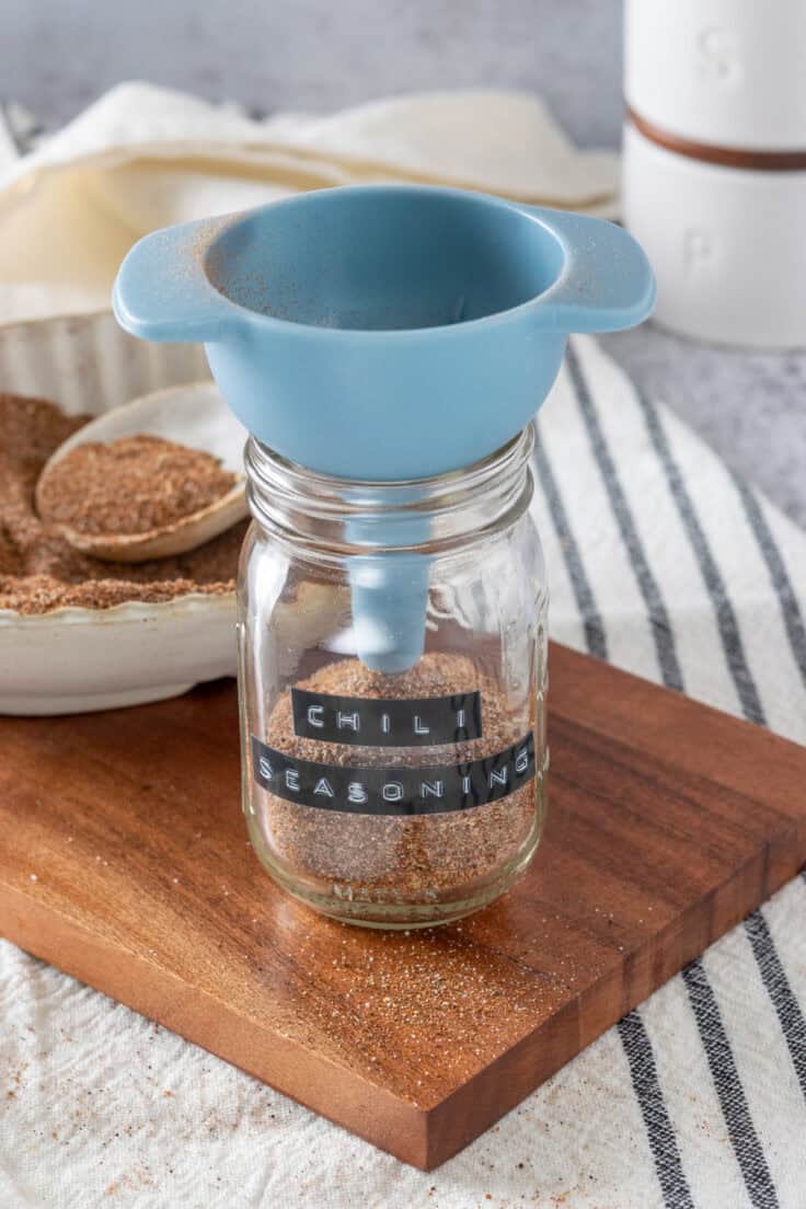 Homemade chili seasoning being funneled into a mason jar.