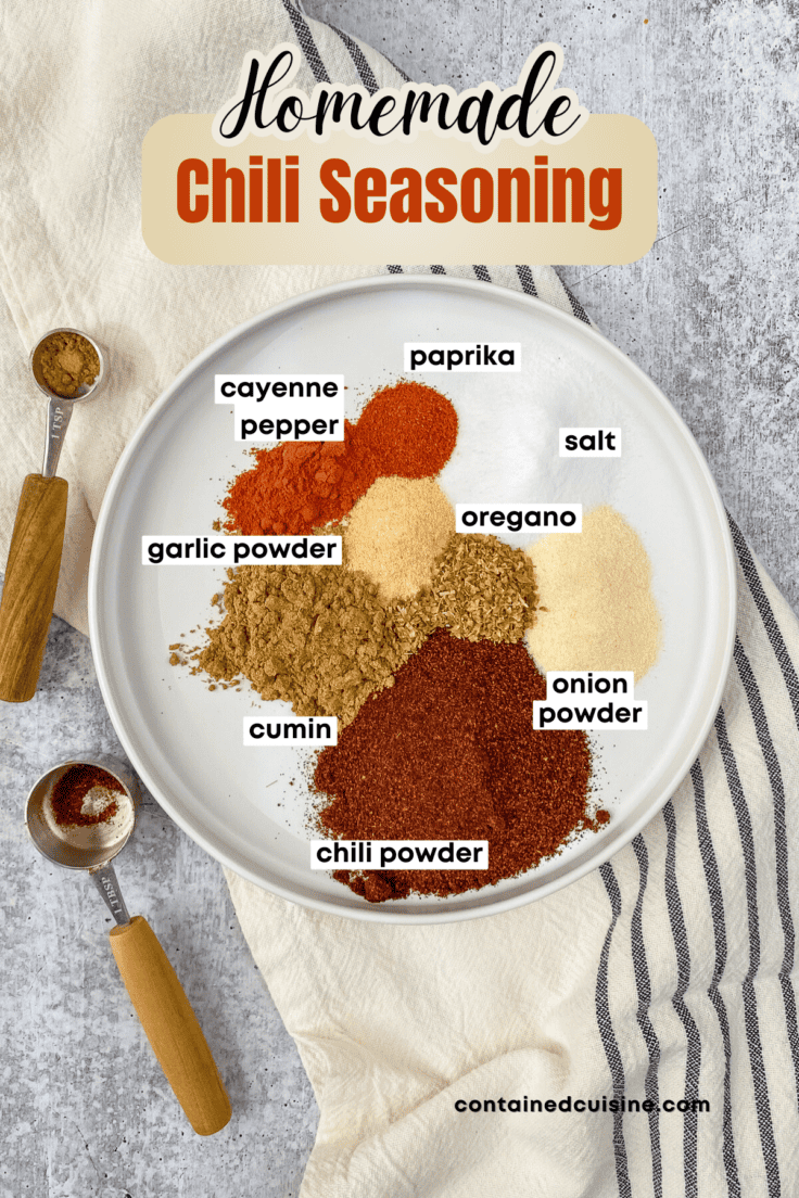 All the spices needed to make chili seasoning mix piled on a round plate that's sitting on a striped kitchen towel. The image has a text overlay that says, homemade chili seasoning.