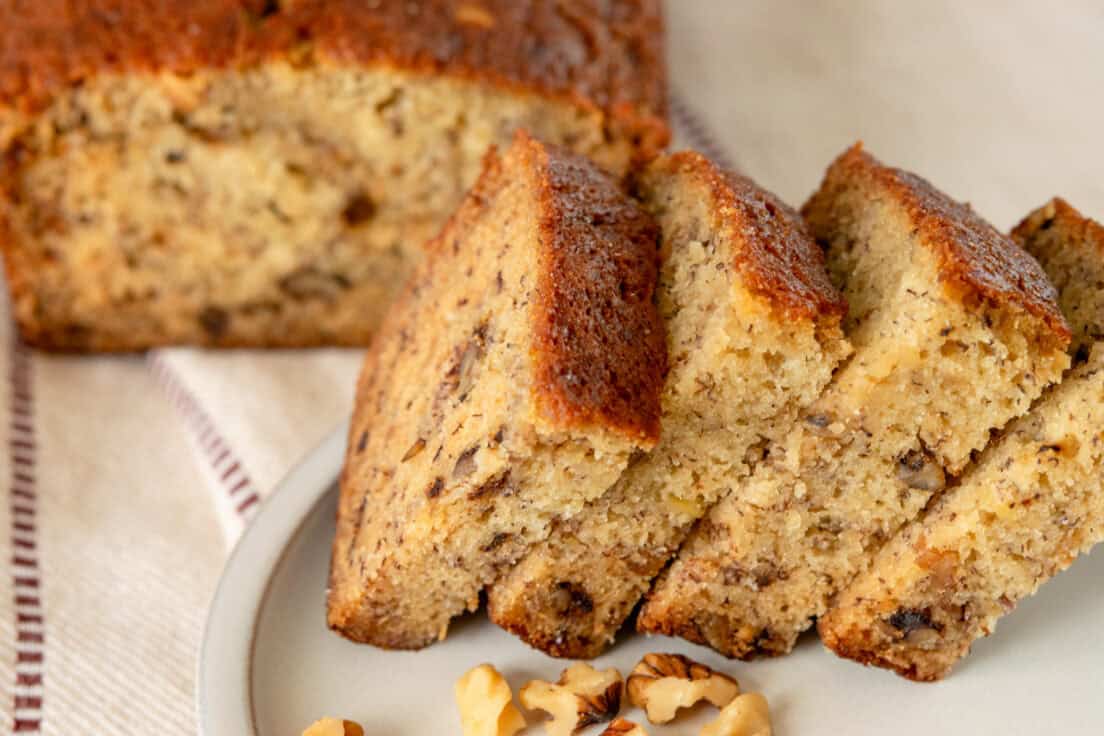 A loaf of banana bread and four slices leaning against it showing how moist the inside is.