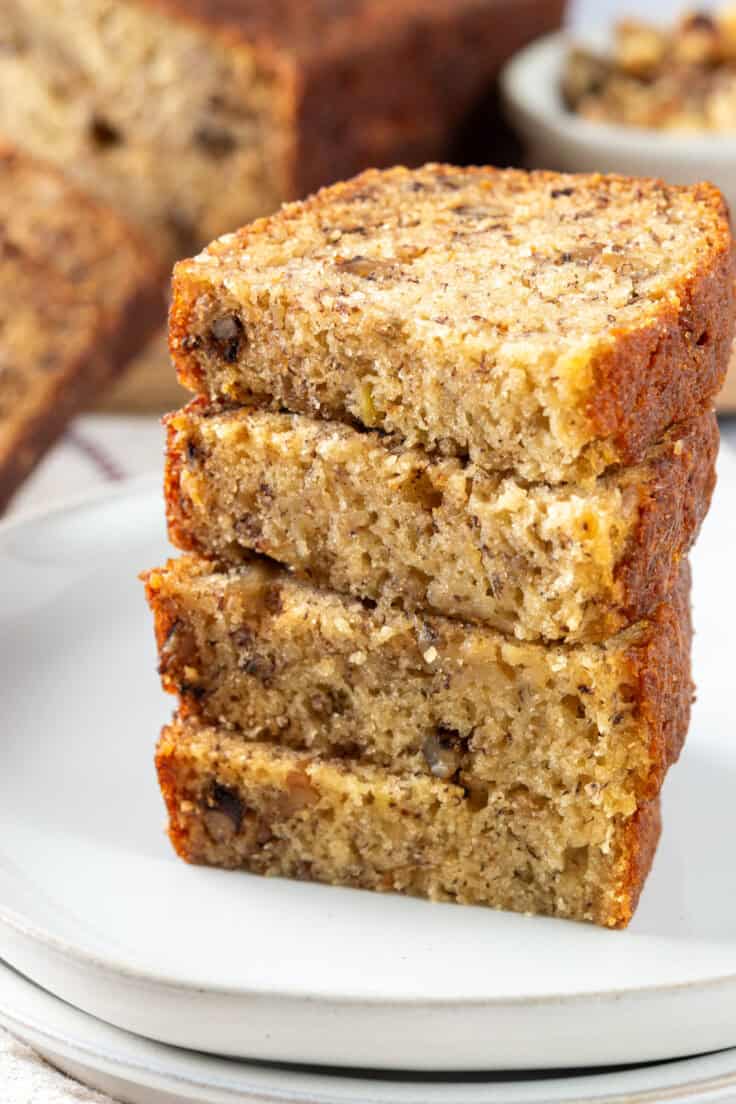 Slices of homemade banana bread stacked on a plate showing the moist inside of the bread.