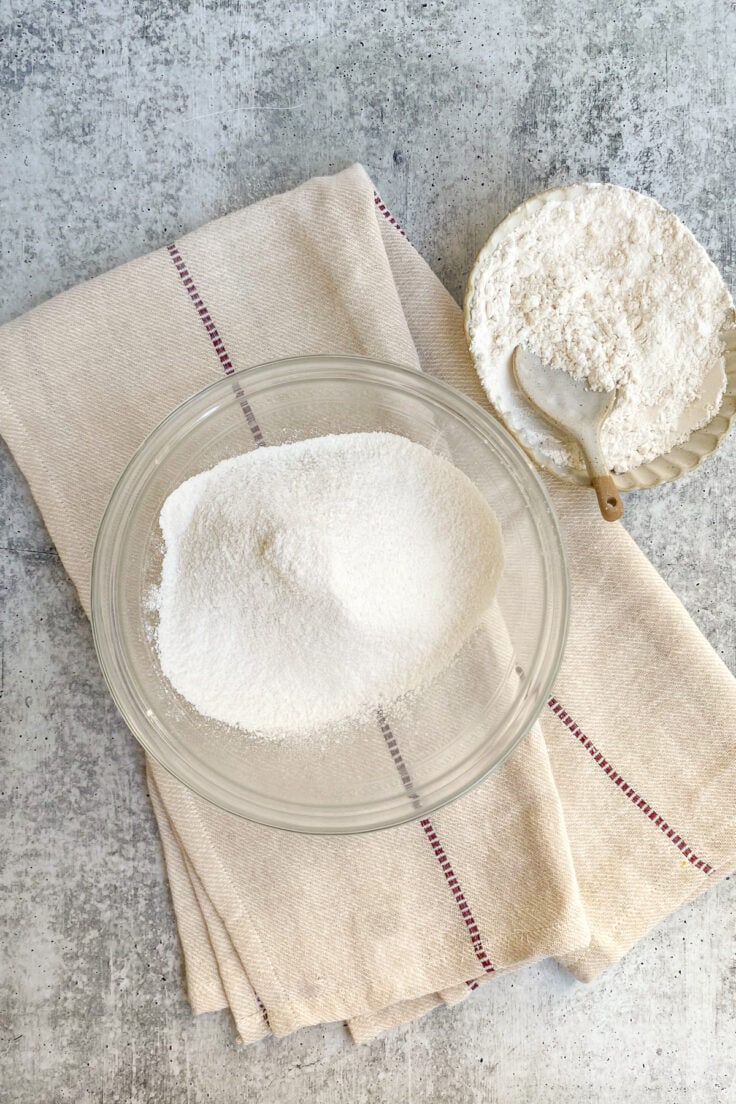 Sifted flour in a bowl that’s sitting on a kitchen towel.