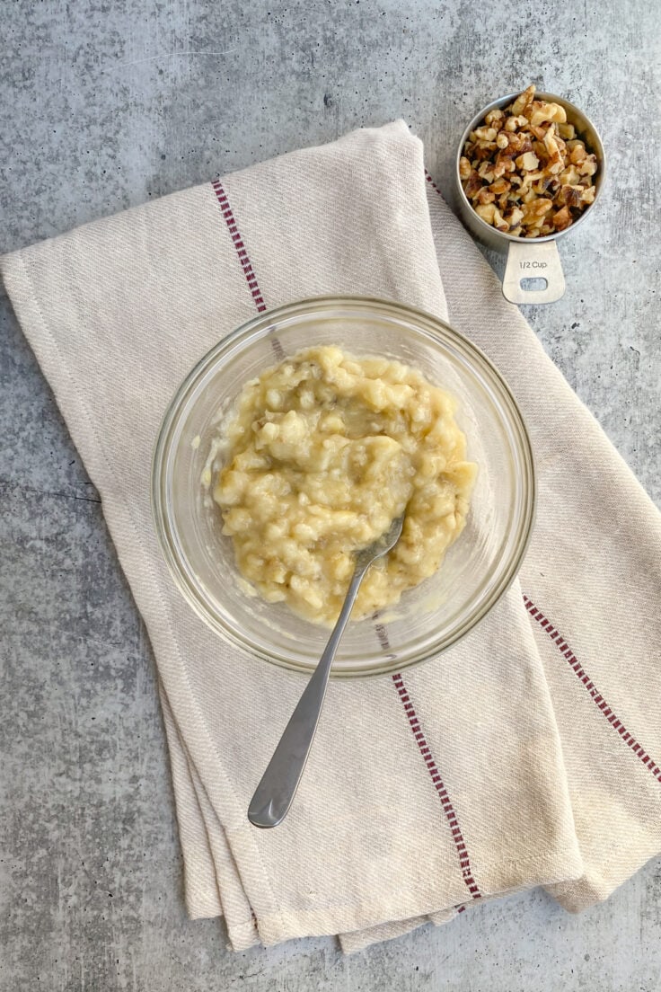 Banana being mashed in a bowl with a fork.