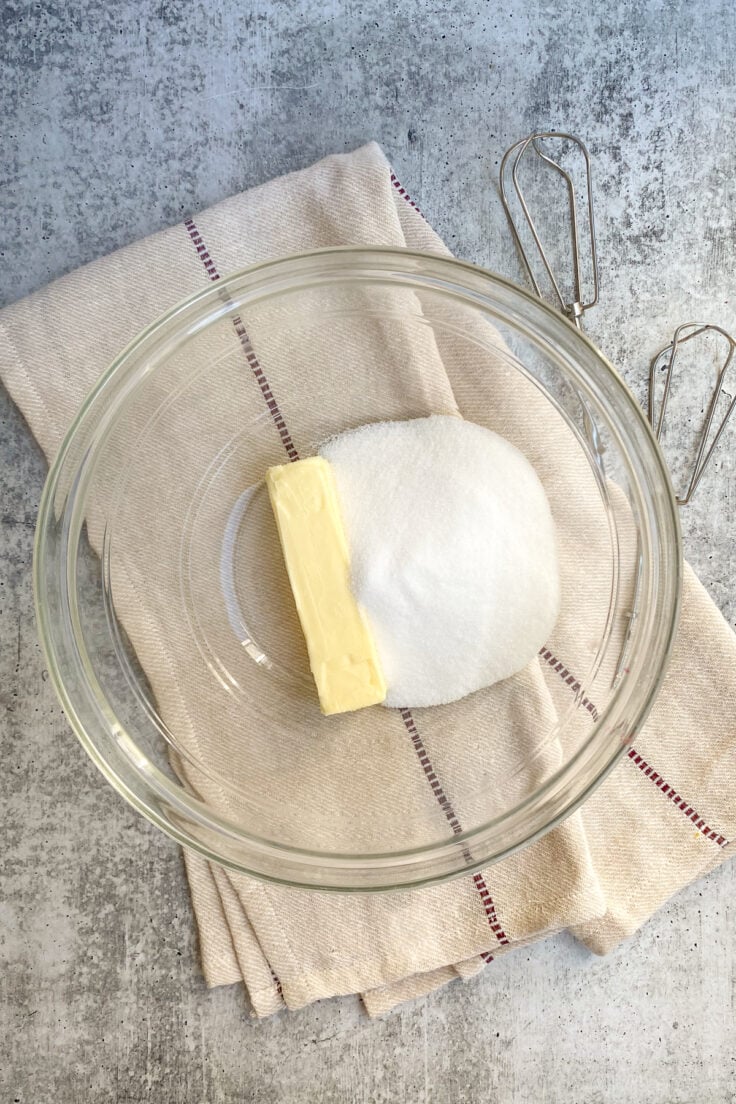 A stick of butter and granulated sugar in a mixing bowl.