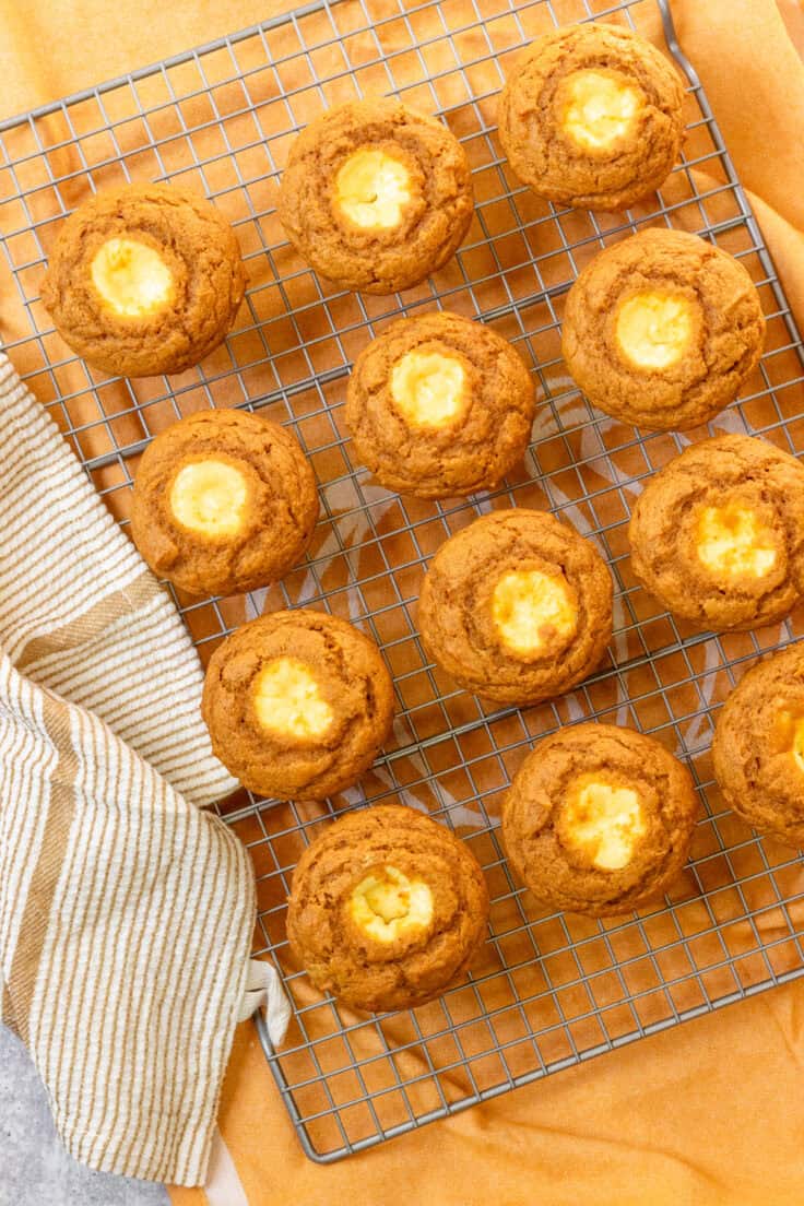 A dozen baked pumpkin muffins with cream cheese filling in the center, cooling on a rack.