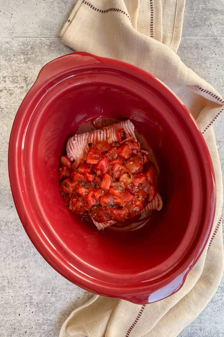 Canned diced tomatoes and tomato paste added to slow cooker to make chili.