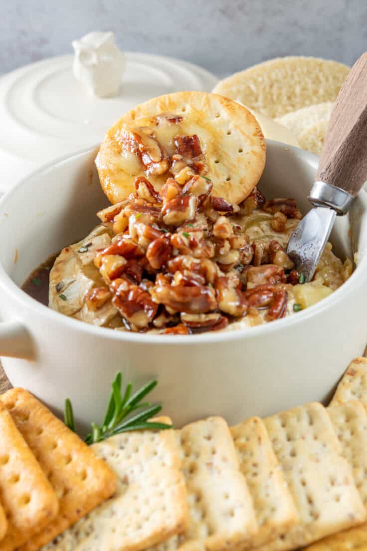 Baked brie spread onto a cracker with lots of pecans and maple syrup on it.