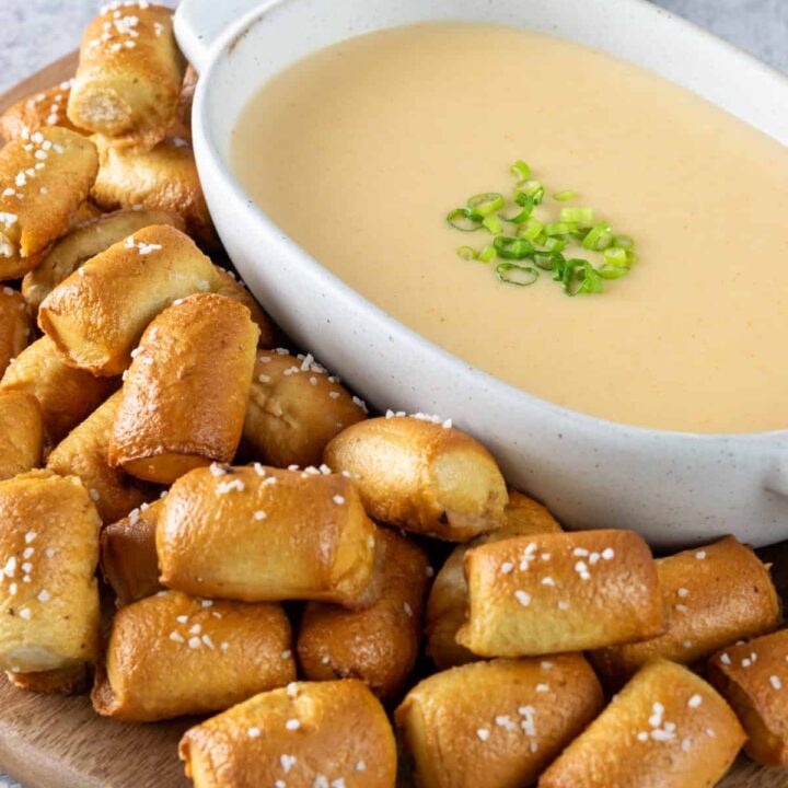 Homemade beer cheese dip in a dipping sauce bowl on a tray surround by pretzel bites for dipping.