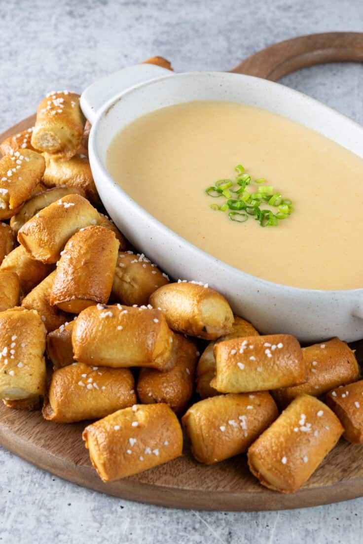 Homemade beer cheese dip in a dipping sauce bowl on a tray surround by pretzel bites for dipping.