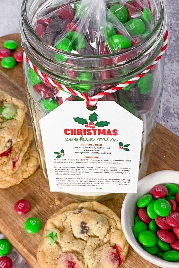 Cookie mix gift in a jar that has red and green m&m's on top, with a gift tag that says, Christmas cookie mix. The gift jar is next to a batch of homemade Christmas cookies and a small bowl full of red and green holiday m&m's.