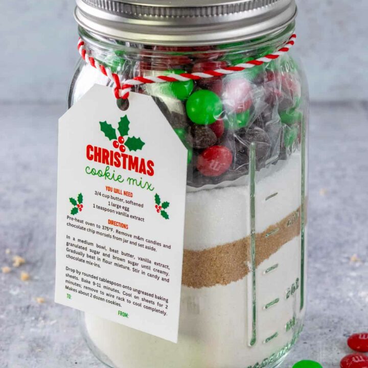 Homemade Christmas Cookie Mix layered in a mason jar that has a printable gift tag on it and some red and green holiday m&m's scattered around the jar.