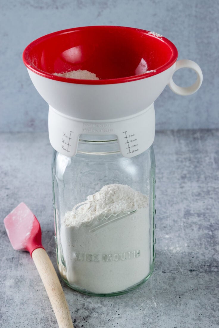 A mason jar with a canning funnel on top that has four added to it.