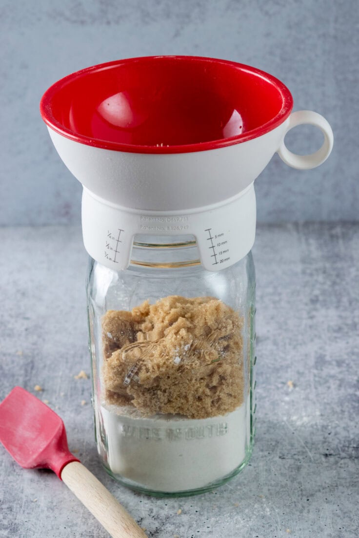 A canning funnel on top of mason jar with brown sugar on top of the flour layer.