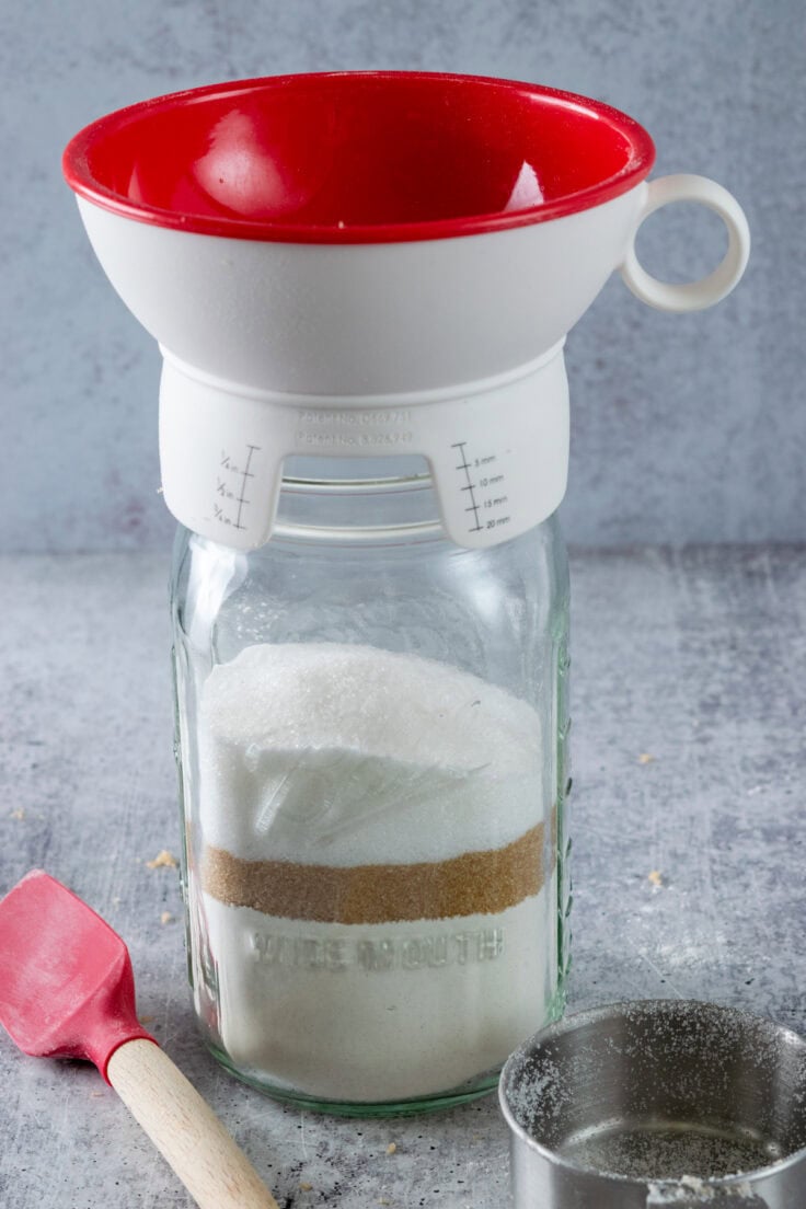 A canning funnel on a mason jar that's being filled sugar to make cookie mix.