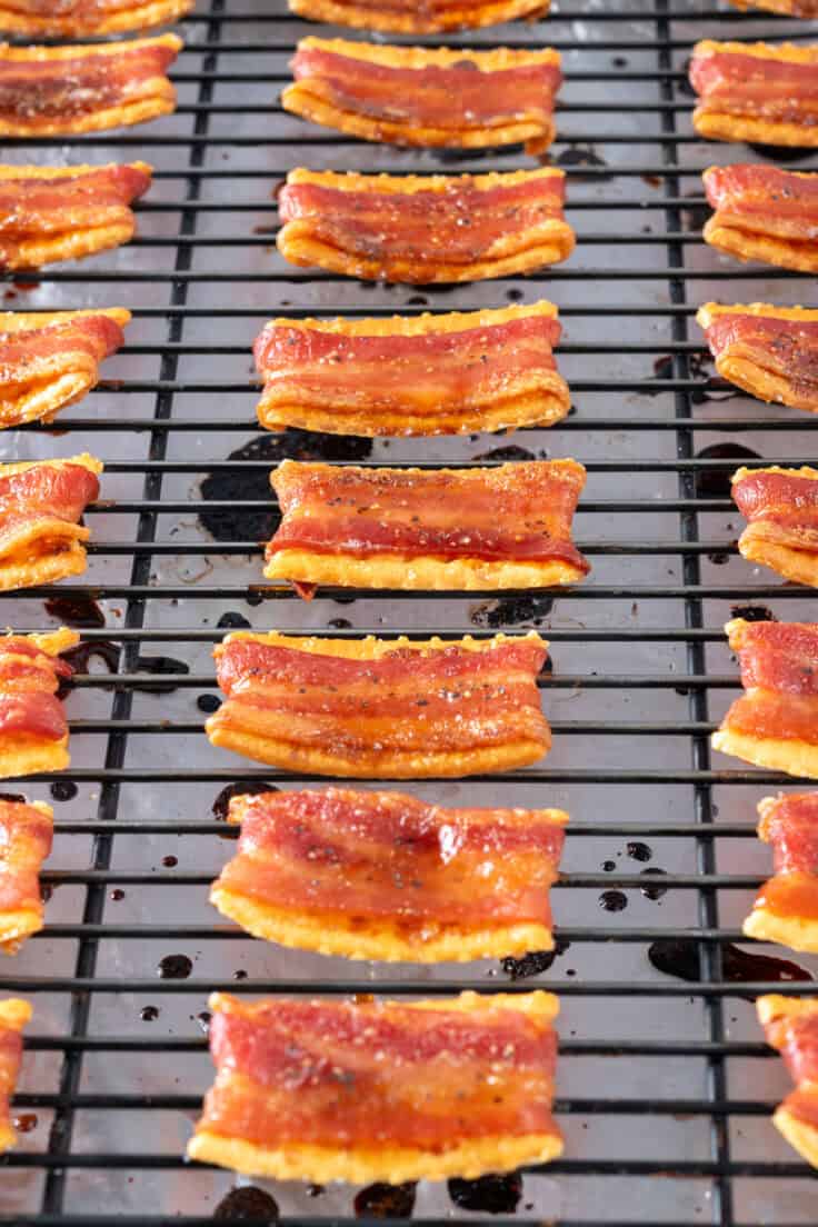 A close-up view showing the cooked bacon crackers still on the baking rack with the bacon all crisp, the edges of the crackers slightly curled up and bits of course ground black pepper.