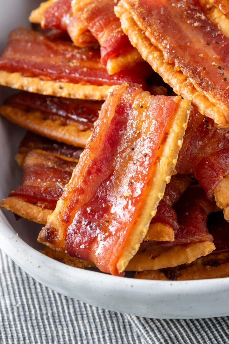 A close up view of bacon crackers in a bowl showing flecks of brown sugar and pepper on the hot, crispy bacon.