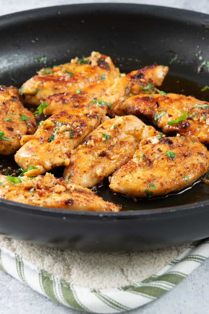 Close up view of honey garlic chicken tenders still in the skillet after cooking, and looking juicy with lots of minced garlic all over.