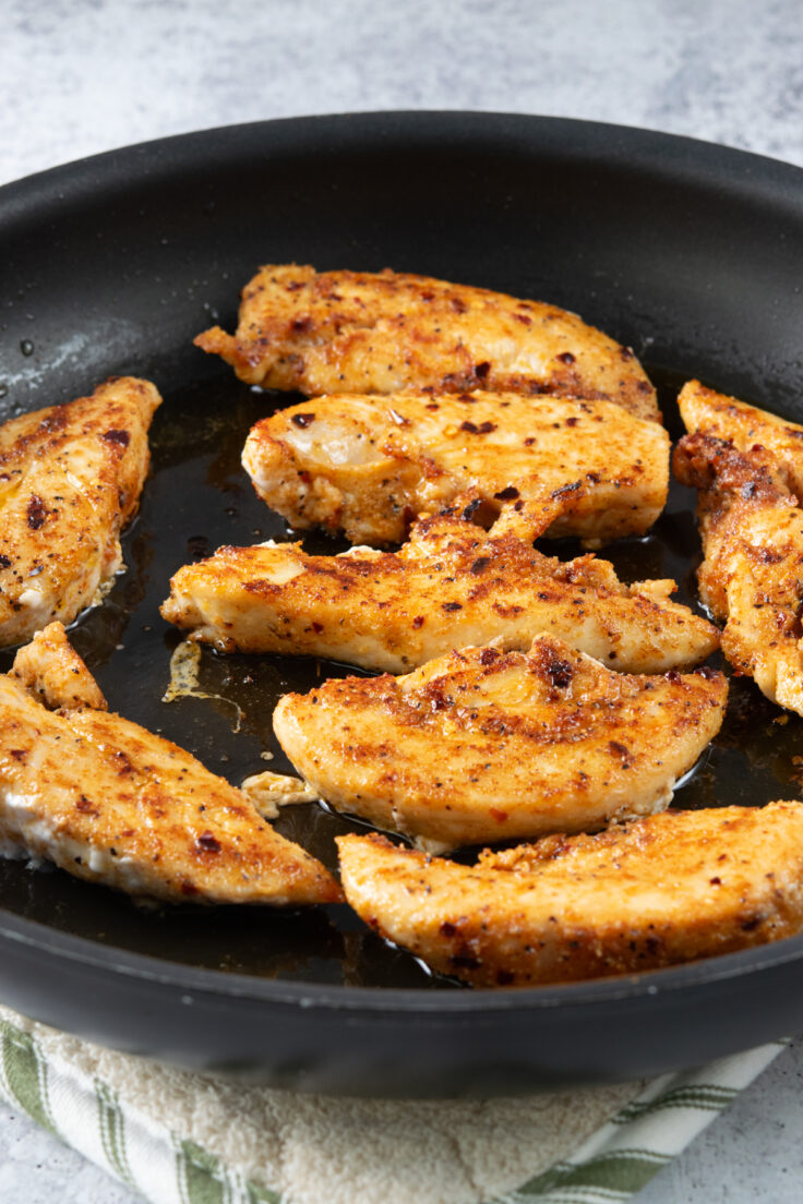 Chicken tenderloins that have been cooked on one side and flipped over to sear the other side.