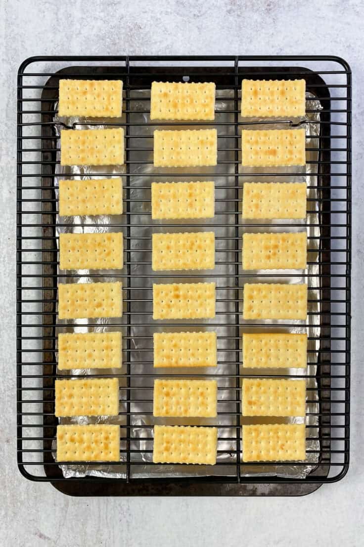 Twenty-four club crackers evenly spaced on a rack which is resting on a foil-lined baking sheet.