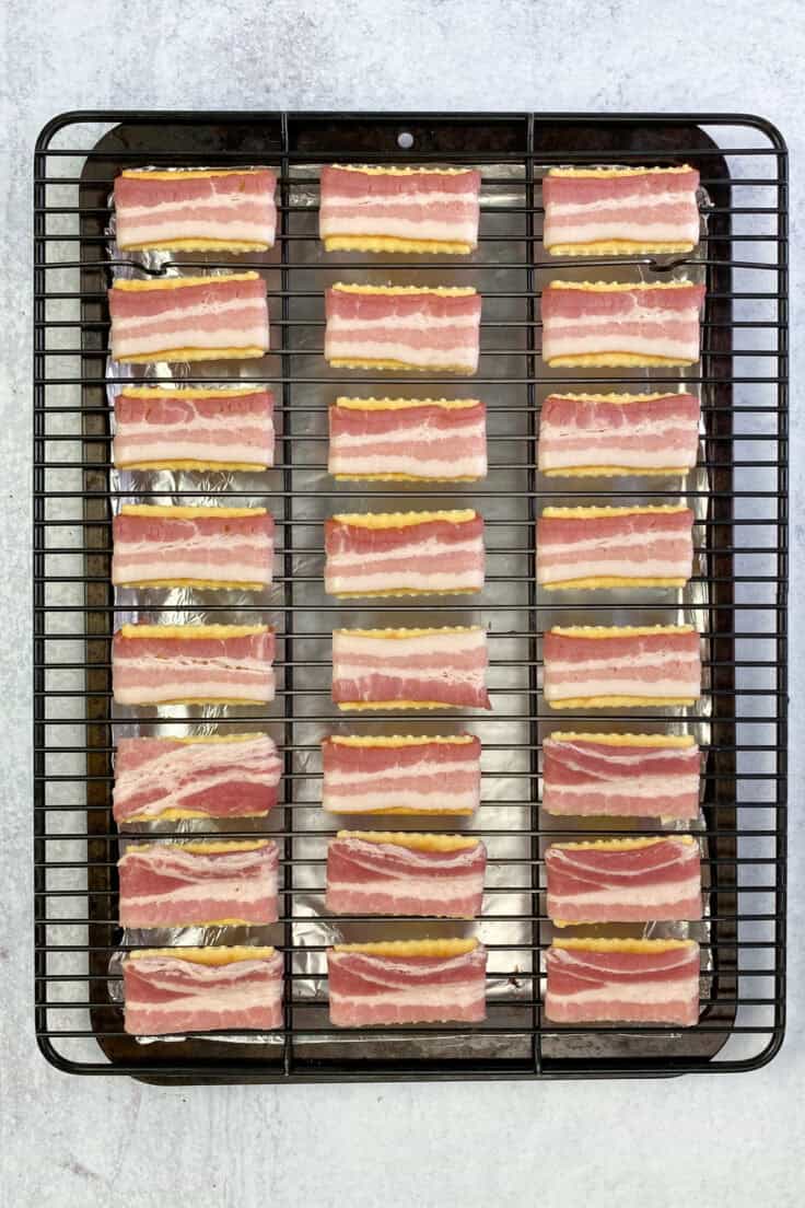 Bacon wrapped across the top and around the edges of each of the twenty-four crackers on the baking rack.