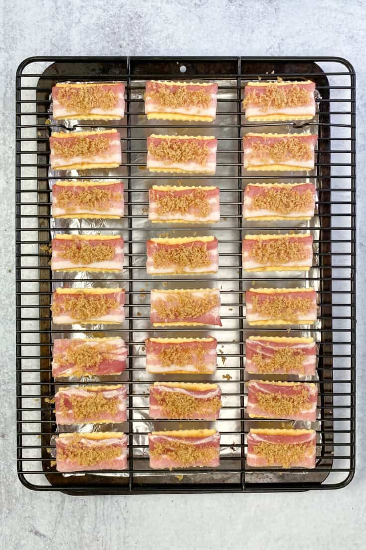 Brown sugar spread across each little piece of bacon on top of each club crackers. The twenty-four bacon club crackers are spread evenly on a baking rack before being cooked.