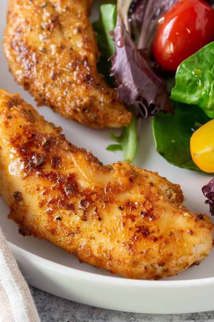 Crispy and juicy chicken tenderloins cooked in olive oil and spices on a plate with a salad.