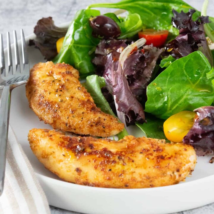 Two pan-seared chicken tenders on a plate with a salad.