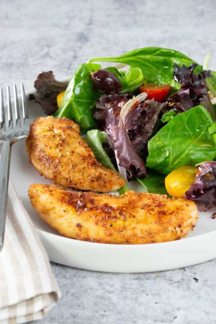 Two pan-seared chicken tenders on a plate with a salad.