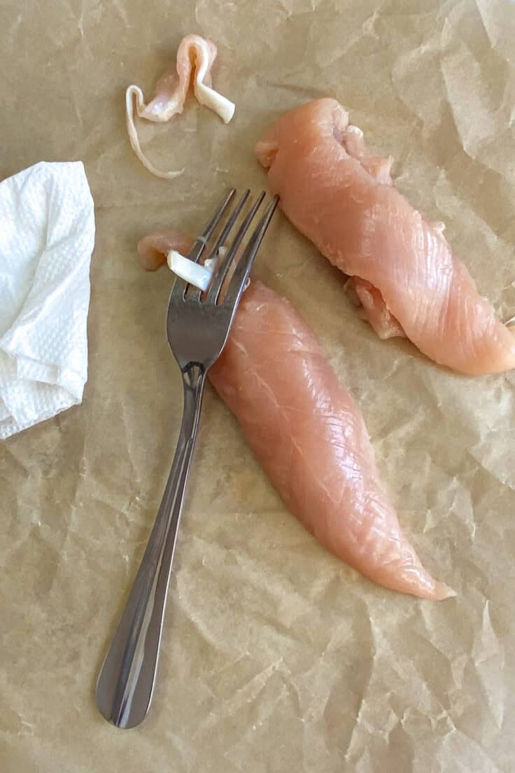 Removing the tendon from a chicken tenderloin with tendon placed between tines on a fork and being pulled by grasping it with a paper towel.