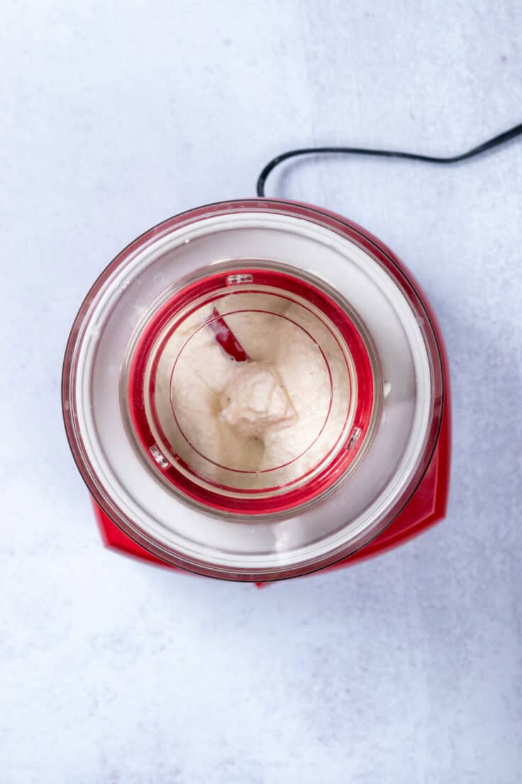 A red Cuisinart automatic ice cream maker that's thickening the vanilla ice cream base.