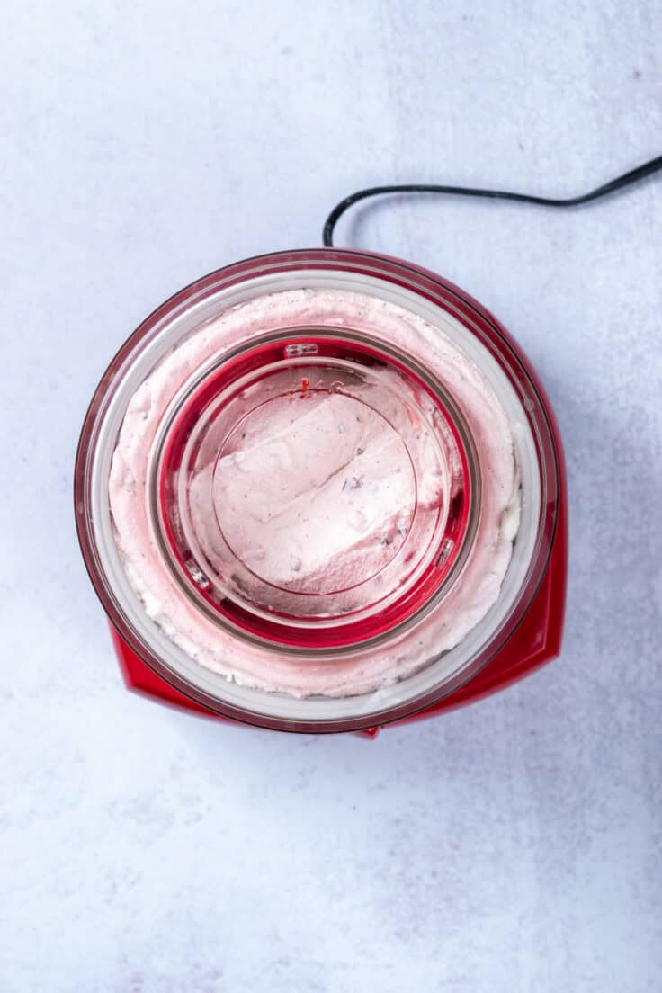 An overhead view of a red Cuisinart automatic ice cream maker that's making homemade Cherry Garcia ice cream.