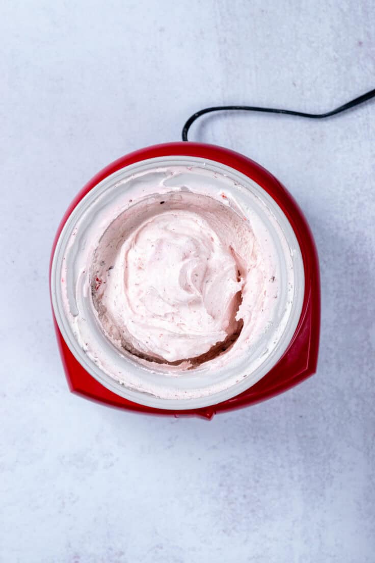 An overhead picture of the finished cherry chocolate ice cream still in the ice cream freezer bowl showing how the ice cream is a little pink with chunks of cherries and flecks of chocolate.