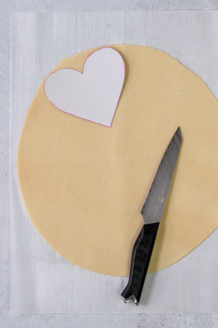 A pie crust with a heart shaped template and sharp knife.