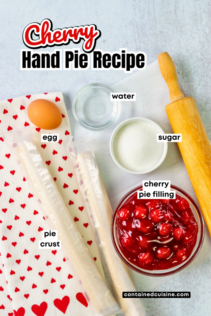 An overhead picture showing all the ingredients needed to make this cherry hand pie recipe, including two Pillsbury pie crusts, cherry pie filling, and egg and small bowls containing water and sugar.