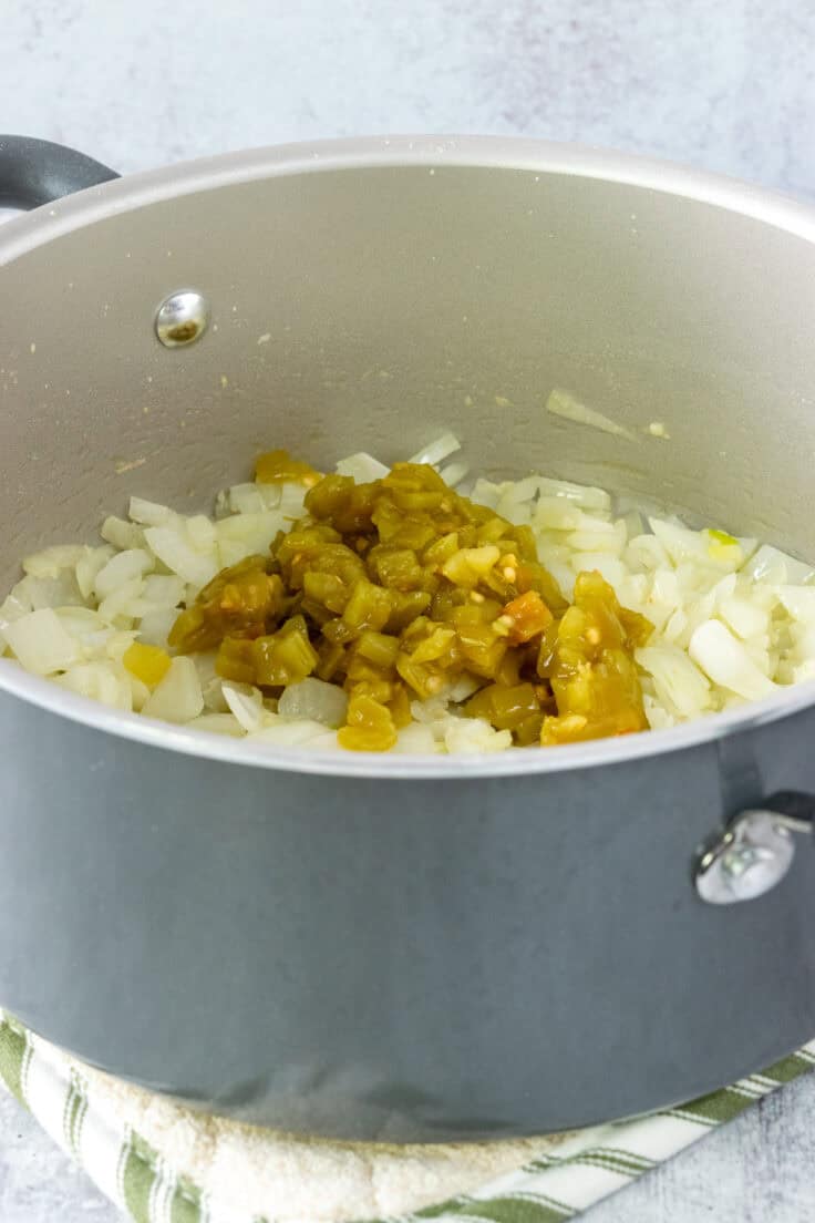 Cooking onion, garlic and diced green chiles in a pot, to make tortilla soup.