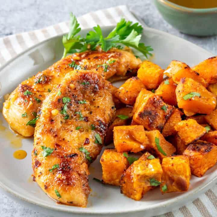 Honey garlic chicken tenders on a plate with roasted vegetables which is next to a small bowl with honey in it.