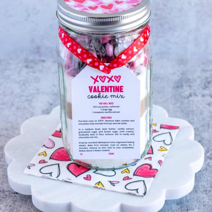 Homemade Valentine Cookie Mix in a mason jar to give as a gift with a gift tag tied on it with some heart ribbon for Valentine's Day.