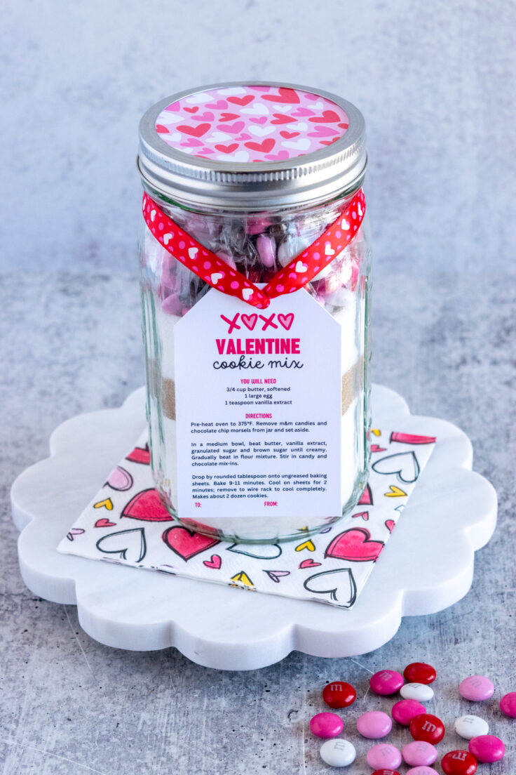 Homemade Valentine Cookie Mix in a mason jar to give as a gift with a gift tag tied on it with some heart ribbon for Valentine's Day.