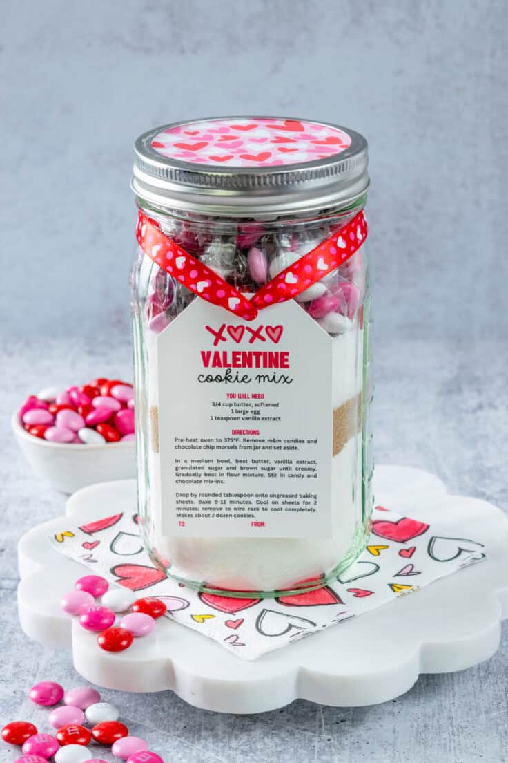 Homemade Valentine Cookie Mix in a mason jar to give as a gift with a gift tag tied on it with some heart ribbon for Valentine's Day.