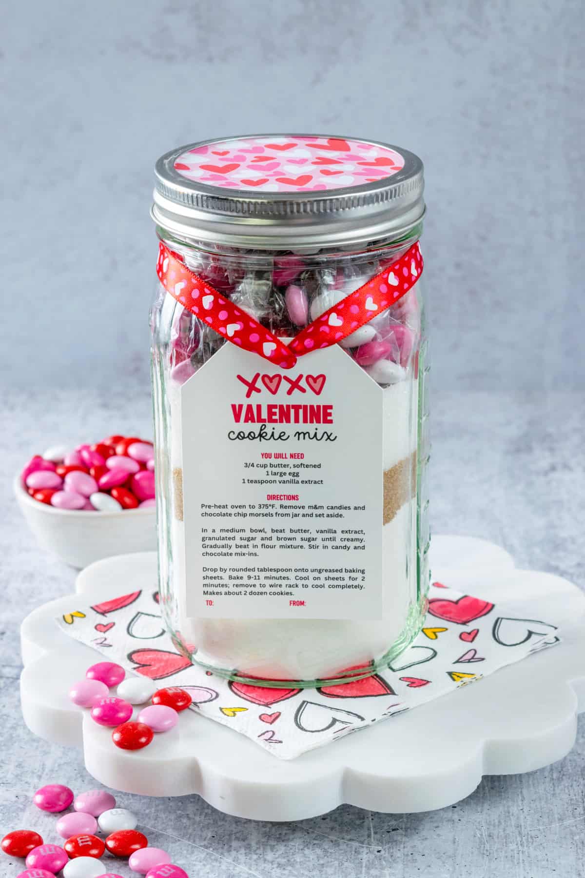 Homemade Valentine Cookie Mix in a mason jar to give as a gift with a gift tag tied on it with some heart ribbon for Valentine's Day.