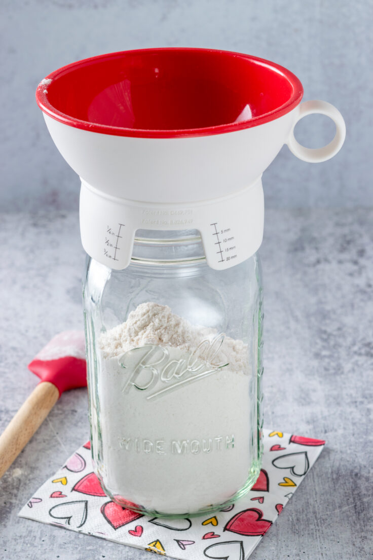 A mason jar with a canning funnel with flour being poured in.