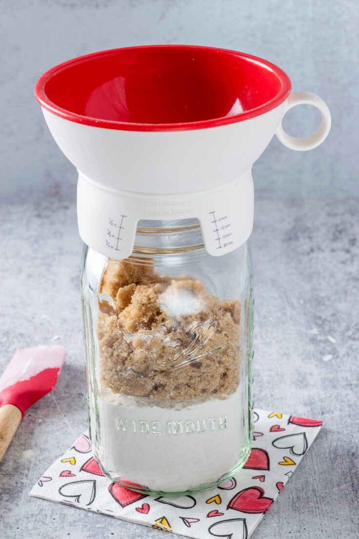 A canning funnel on a mason jar that has flour in it and is being filled with brown sugar.