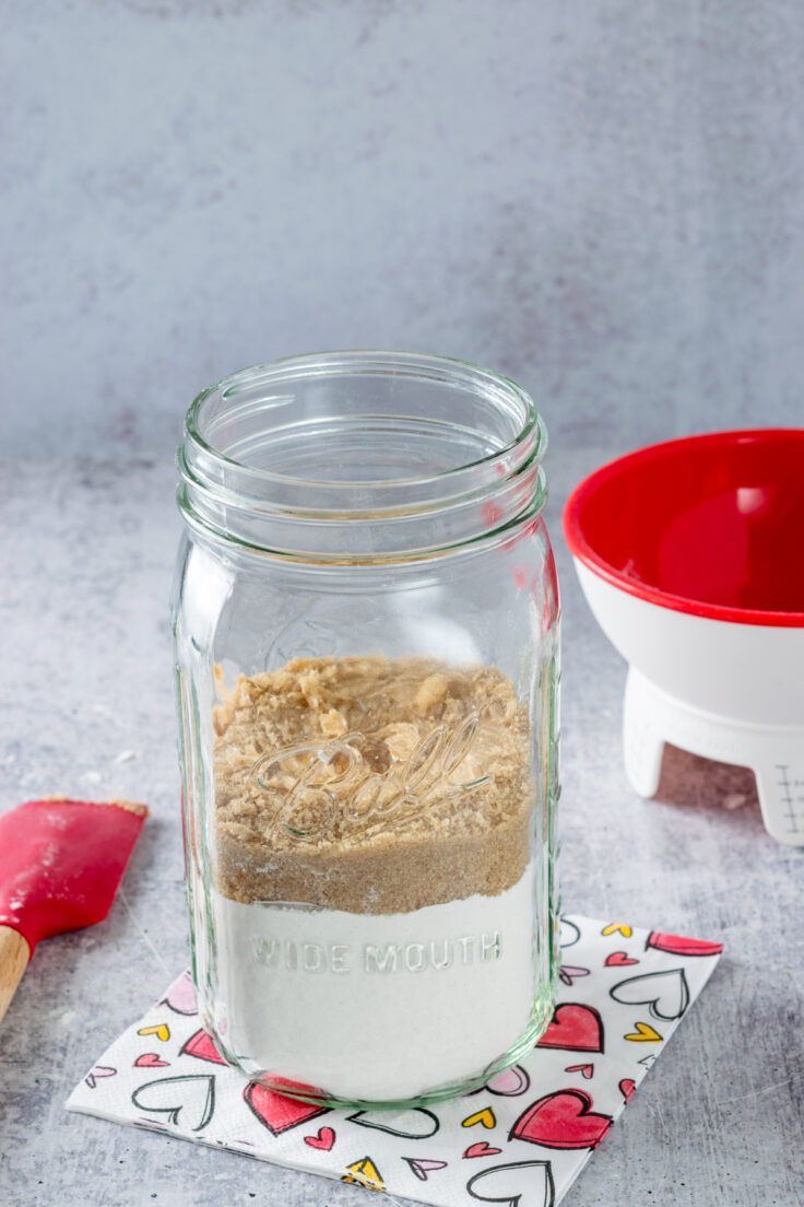 A mason jar with flour and brown sugar that's being made into cookie mix in a jar.