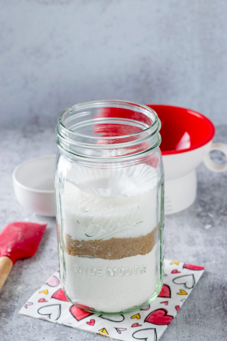 Making cookie mix in a mason jar and showing how the sugar level is leveled off before adding the next ingredient.