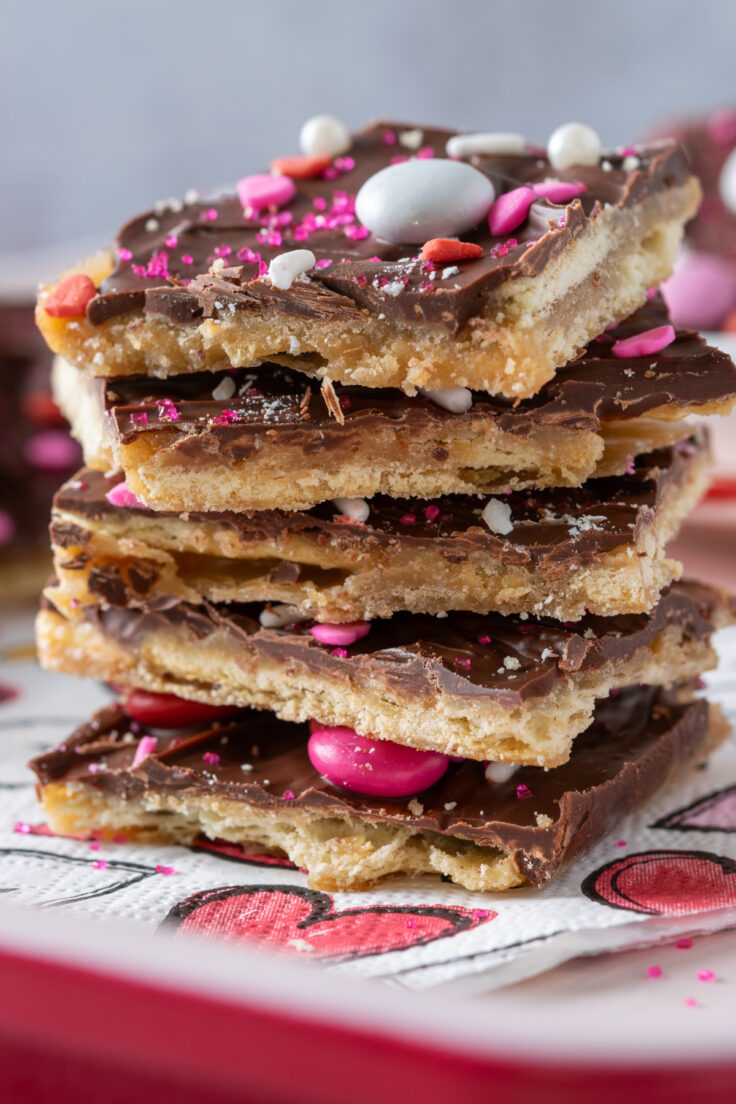 Mouth-watering picturing of five pieces of Cupid Crack Candy stacked up showing the layers of saltine crackers, toffee, chocolate, and Valentine's Day sprinkles.