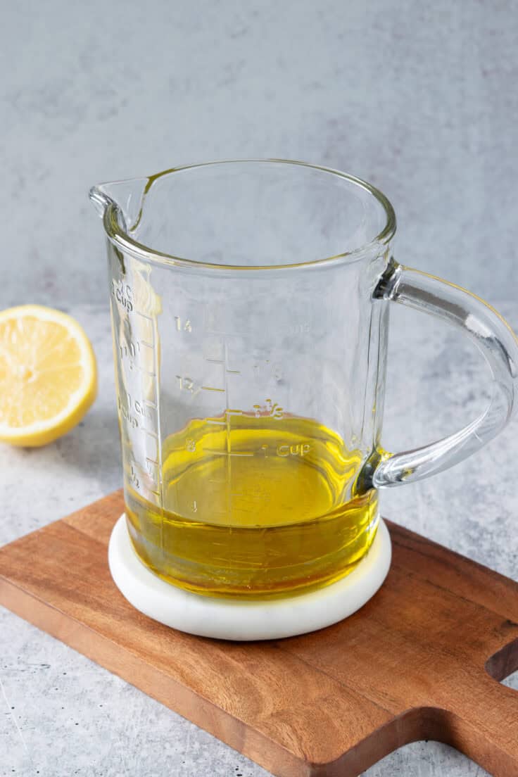 Making homemade lemon salad dressing in a large glass measuring cup which has olive oil in it.