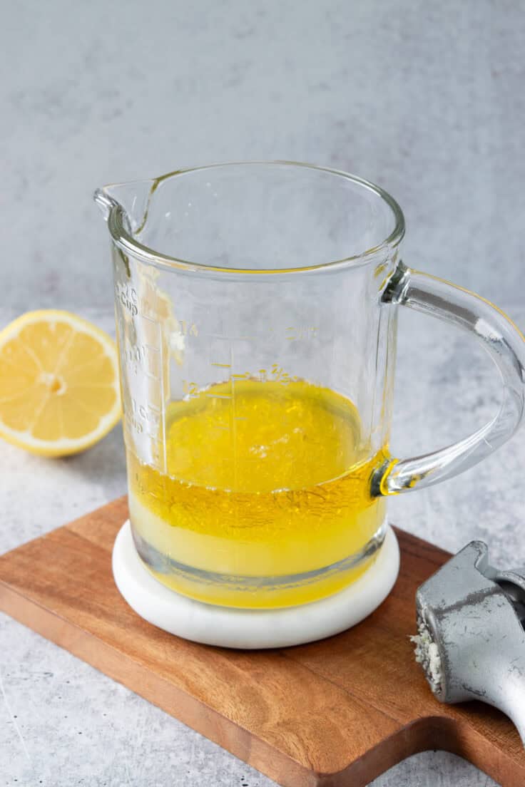  A garlic press next to a large measuring cup used to make lemon salad dressing, that has olive oil, lemon juice and minced garlic in it.