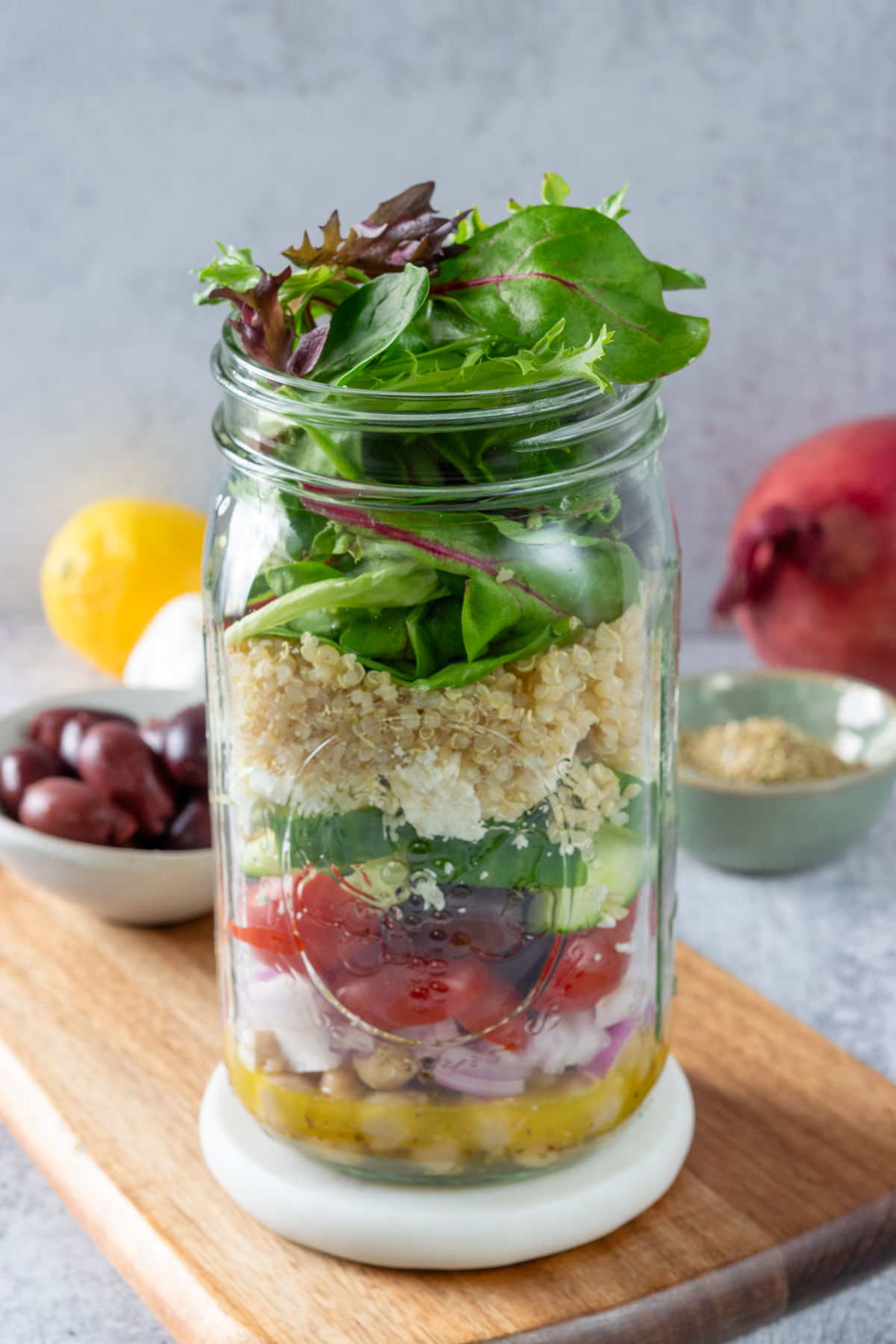 A Mediterranean salad packed in a mason jar with layers of lemon dressing, onion, tomatoes, cucumber, olives. feta cheese, quinoa and salad greens.